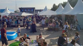 Tents, stands and a stage in the background. In the foreground, people are eating and children are playing near a paddling pool.