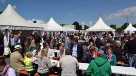 Information and family day around the Infobox: People are sitting on benches and eating. In the background, there are campaign tents and stands.