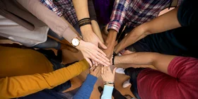 [Translate to Englisch:] Viele Hände aufeinander gelegt in der Mitte des Bildes als Symbol für Teamwork