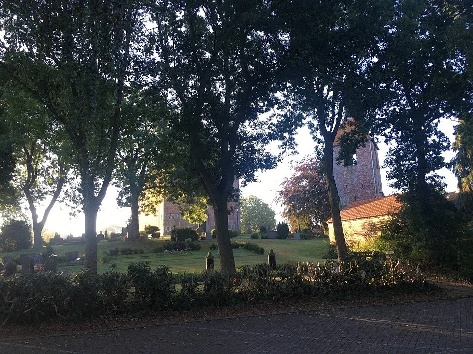 Das Foto zeigt die historische Etzeler Kirche hinter malerischen Bäumen auf dem „hohen Warfland“: Nun ist es Zeit für den Endspurt auf den letzten beiden Kilometern die Etzeler Dorfstraße und den Moorstricher Weg entlang