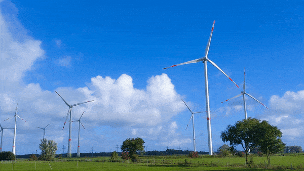 Three spinning wind turbines on a field against blue sky